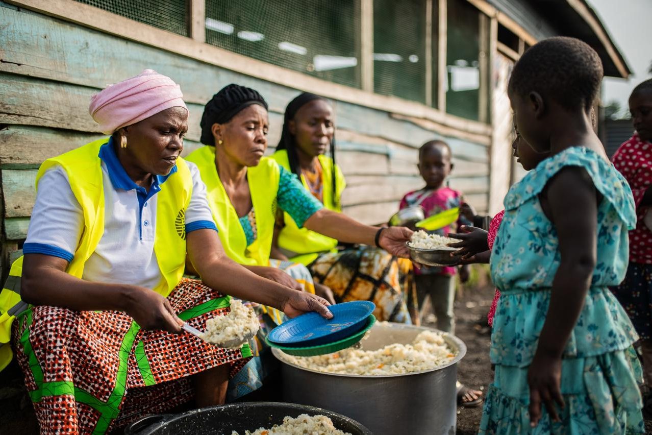 Volunteers in high-visibility vests serving prepared food to a child at the distribution point.